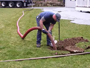 Septic pumping technician servicing a residential septic tank with a vacuum hose in Lexington, MA