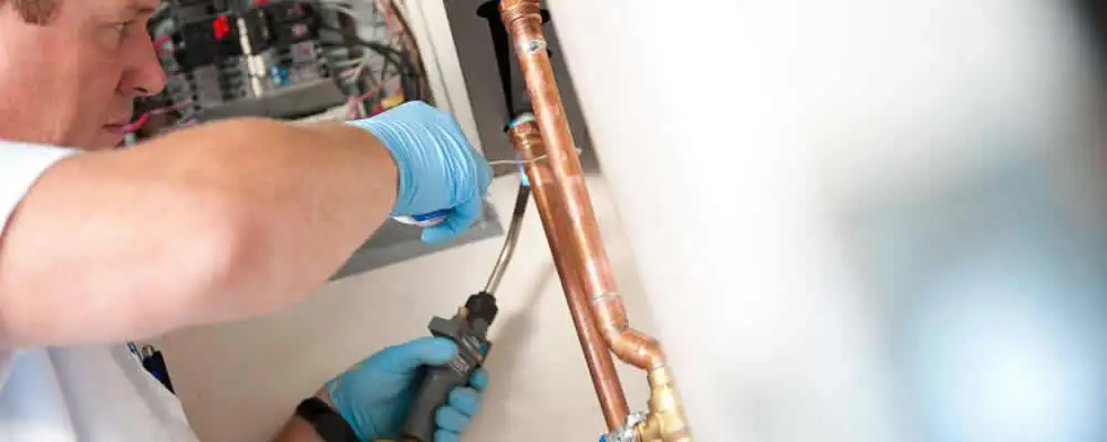 Water heater repair technician testing copper pipe connections and controls in Lexington, MA